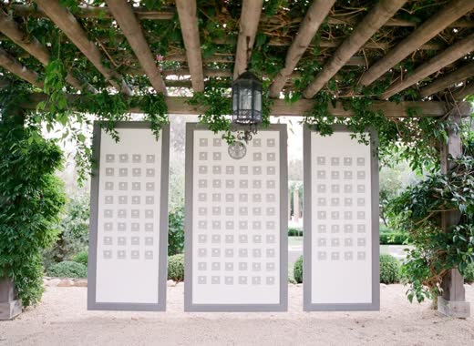 Framed seating chart panels under a trellis of greenery