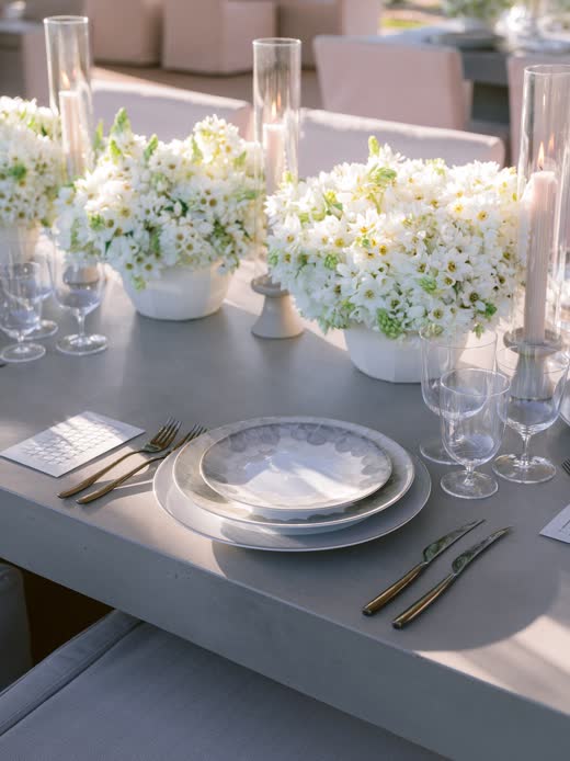 A white table set with layered plates and white flowers