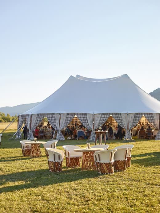 A sailcloth tent and lounge seating on a lawn at golden hour